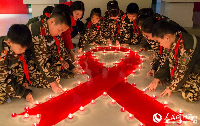 呼和浩特市玉泉区五塔寺东街小学学生用蜡烛点亮红丝带,纪念世界艾滋病日。