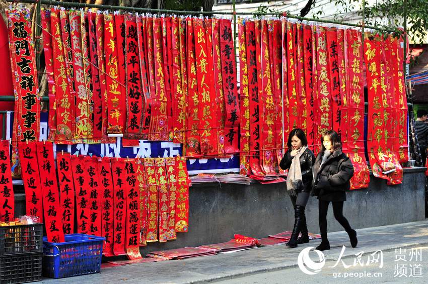 2019年1月26日，在贵州省黔东南苗族侗族自治州从江县年货节上，两名姑娘经过一个春联摊位。梁光源 摄