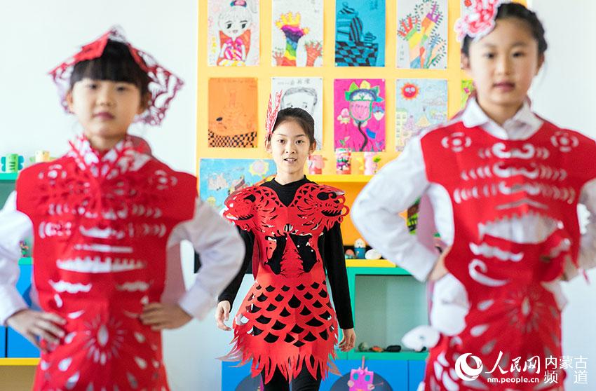 呼和浩特市玉泉区恒昌店巷小学剪纸社团的学生在展示创意剪纸服饰。