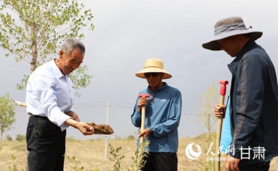 天气干旱，郭万刚(左一)来到治沙点，捧起一抔土，和林场工人一起查看墒情。人民网 王文嘉摄