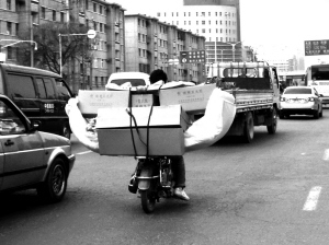 一市民骑无牌摩托车载托运数箱重物穿梭车流中